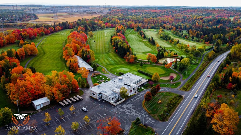 Aerial view of a commercial building surrounded by autumn foliage, green fields, and a highway in a rural landscape