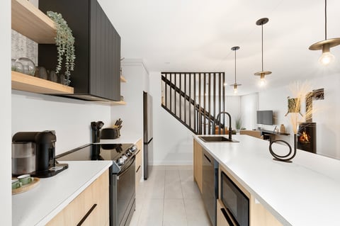 Modern galley kitchen with white counters, light wood and black cabinetry, stainless steel appliances, and pendant lighting