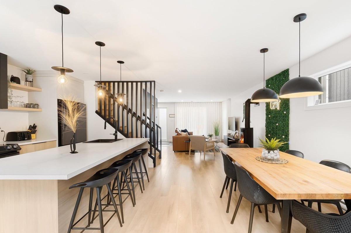 Modern open-plan kitchen and dining area with white cabinetry, wood table, black bar stools, and pendant lighting