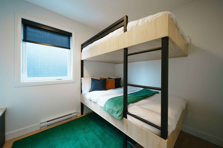 Modern bedroom with black-framed bunk bed with cream mattresses, green floor, and window with blue blinds