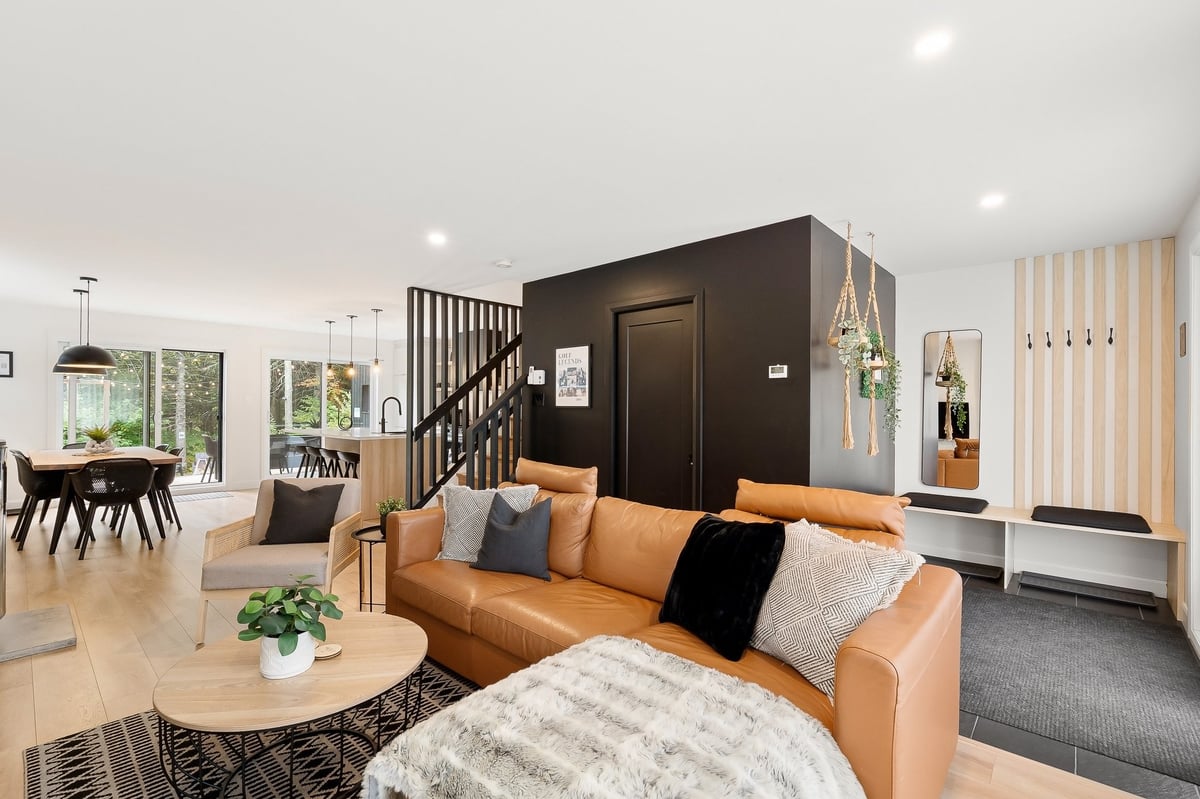 Modern open-concept living room with tan leather sectional, black staircase, and dark accent wall in contemporary home