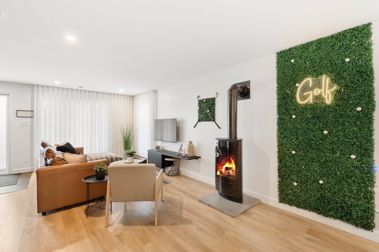 Modern living room with orange sofa, black stove fireplace, artificial green wall with gold neon sign, and wooden flooring