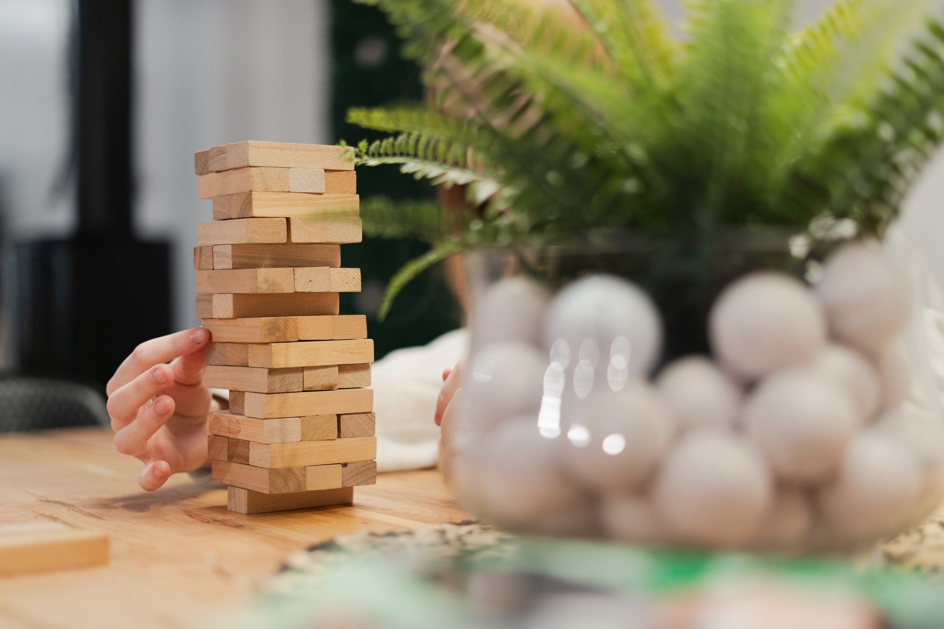 Hand holding stacked wooden blocks tower with dice and potted plants blurred in background on wooden table